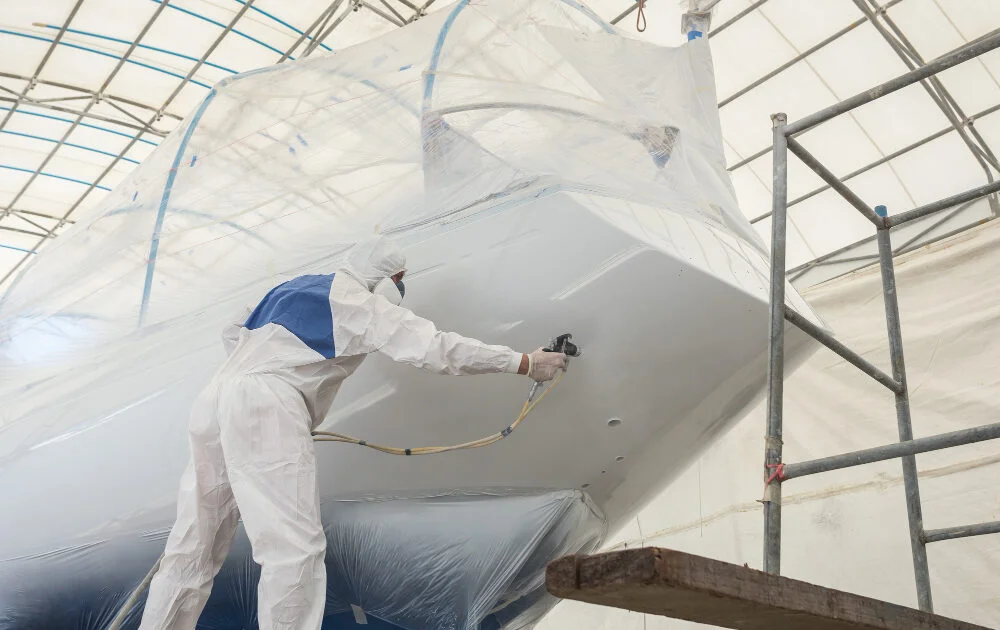 worker wearing protective uniform spraying paint boat 1000x630 1 - Farby antykorozyjne dla przemysłu morskiego – właściwości, zastosowanie, wyzwania.